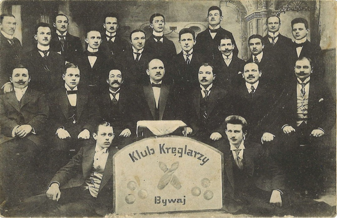 Fotografia przedstawiająca grupę mężczyzn. Przed nimi tablica z napisem klub kręglarzy bywaj.